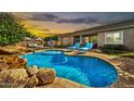 Beautiful pool and rock waterfall against the warm sunset, surrounded by landscaping and comfortable seating at 9388 W Cashman Dr, Peoria, AZ 85383