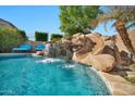 Gorgeous pool featuring a rock waterfall and slide, surrounded by lush landscaping and comfortable lounge chairs at 9388 W Cashman Dr, Peoria, AZ 85383