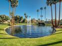 Scenic pond with a fountain surrounded by lush green grass and tall palm trees at 9707 E Mountain View Rd # 1456, Scottsdale, AZ 85258