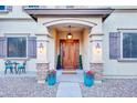 Elegant front entrance showcasing a beautiful wood door, stone accents, and colorful floral arrangements at 11737 N 143Rd Dr, Surprise, AZ 85379