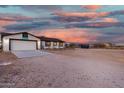 Single-story home featuring a two-car garage and large dirt lot under a vibrant sunset sky at 20438 W Carver Rd, Buckeye, AZ 85326