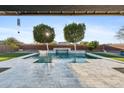 Beautiful pool with a cascading water feature, lush landscaping, and a clear blue sky at 12962 N 145Th Ave, Surprise, AZ 85379