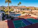 Aerial view of a backyard featuring a pool, sport court, mature landscaping, and mountain views at 10301 N 128Th St, Scottsdale, AZ 85259