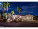 Striking home exterior at night, showcasing lush landscaping and a welcoming two-car garage at 22329 N Padaro Dr, Sun City West, AZ 85375
