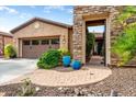 Charming exterior with a two-car garage, stone entryway, lush greenery, and decorative blue planters at 29412 N 128Th Ln, Peoria, AZ 85383