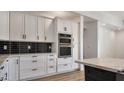 Close-up of kitchen with sleek black backsplash, white cabinets, and stainless steel double ovens at 11612 S 211Th Ln, Buckeye, AZ 85326