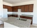 Open kitchen featuring granite countertops, an island with a sink, and brown wooden cabinetry at 25180 W Wayland Dr, Buckeye, AZ 85326