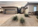 Home exterior featuring a three car garage, desert landscaping, stone accents, and a brick paver driveway at 6039 E Sienna Bouquet Pl, Cave Creek, AZ 85331