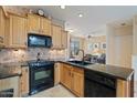 Kitchen boasts wooden cabinetry, stone backsplash, black appliances, and granite countertops at 9718 E Boston St, Mesa, AZ 85207