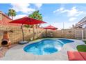 Backyard with a refreshing pool, red patio umbrellas, and a cozy fireplace in a block-walled yard at 4121 E Ashurst Dr, Phoenix, AZ 85048