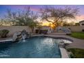 Backyard oasis with a pool, waterfall, spa, and outdoor fireplace with sunset at 7501 E Phantom Way, Scottsdale, AZ 85255