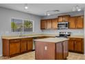 Well-lit kitchen with a practical island, stainless steel appliances, and wood cabinets at 43646 W Elizabeth Ave, Maricopa, AZ 85138