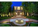 Night view of the front exterior featuring a stone facade, fountain, manicured landscaping, and illuminated trees at 9547 N 55Th St, Paradise Valley, AZ 85253