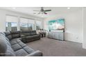 Spacious living room with plush gray sectional, large windows, ceiling fan, and modern entertainment center at 14317 W Faye Way, Surprise, AZ 85387