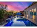 Backyard oasis featuring a sparkling pool, cascading water feature, umbrella covered lounge chairs, and festive string lights at 9183 W Foothill Dr, Peoria, AZ 85383