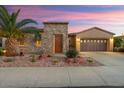 Charming single-story home with a stone accent wall, desert landscaping, a two-car garage, and a beautiful sunset backdrop at 12663 W Pinnacle Vista Dr, Peoria, AZ 85383