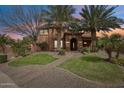 Charming two-story home with desert landscaping, palm trees, and a brick walkway leading to the arched entrance at dusk at 20396 E Via Del Rancho Rd, Queen Creek, AZ 85142