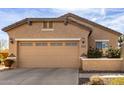 Tan stucco home with a two-car garage featuring decorative fixtures and desert landscaping at 26057 W Sequoia Dr, Buckeye, AZ 85396