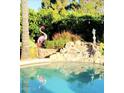 Beautiful pool area with a rock waterfall, tropical plants, and a playful pink flamingo statue at 9360 E Milagro Ave, Mesa, AZ 85209