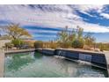 Inviting pool features a tranquil waterfall feature, desert landscaping, and dining set under a striped umbrella at 9565 E Mountain Spring Rd, Scottsdale, AZ 85255