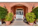 Close-up of a brick entryway that features an arched doorway, detailed door, and ornamental potted plants at 1520 E Elmwood Cir, Mesa, AZ 85203