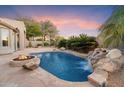 Stunning backyard pool with a rock waterfall feature, a fire pit, and lush desert landscaping at 7111 E Sienna Bouquet Pl, Scottsdale, AZ 85266