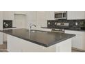 Modern kitchen island with dark countertops, white cabinets, stainless steel appliances, and hexagon backsplash at 12738 N 172Nd Dr, Surprise, AZ 85388