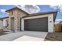 Home exterior featuring a two-car garage, stone accents, and a well-lit entrance under a partly cloudy sky at 7649 W Minton St, Laveen, AZ 85339