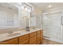 Bathroom featuring double sinks, granite counters, wood cabinetry, and glass-enclosed shower at 19595 N 107Th Dr, Sun City, AZ 85373