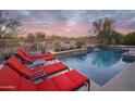 Inviting pool area with lounge chairs and a waterfall feature under a colorful sunset sky at 4251 E Desert Forest Trl, Cave Creek, AZ 85331