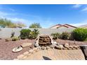 Backyard featuring desert landscaping, waterfall feature, desert plants and a gray block wall for privacy at 15876 W Alpine Ridge Dr, Surprise, AZ 85374