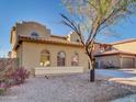 Side view of a two-story home with desert landscaping featuring a mature tree and charming arched windows at 16247 W Desert Mirage Dr, Surprise, AZ 85379