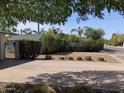 Front yard features a lush hedge, decorative round hay bales, and shade from the trees on a sunny day at 4145 E Libby St, Phoenix, AZ 85032