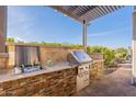Outdoor kitchen boasts stainless steel appliances, a sink, and a grill nestled in a stone counter under a modern pergola at 706 E La Palta St, Queen Creek, AZ 85140