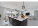 A contemporary kitchen island features dark cabinets, a sink, and views of the adjacent dining and living areas at 20256 W Highland Ave, Litchfield Park, AZ 85340