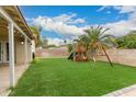 View of the backyard with a wood playset, artificial grass and mature palm tree at 7605 W Avalon Dr, Phoenix, AZ 85033