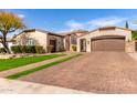 Expansive brick driveway leading to a three-car garage with well-manicured lawn and mature shade tree at 9834 E Voltaire Dr, Scottsdale, AZ 85260