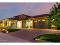 Twilight view of home with manicured front yard, brick driveway, and exterior lighting at 15936 W Bonitos Dr, Goodyear, AZ 85395