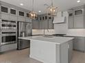 Modern kitchen featuring gray cabinets, a stainless steel refrigerator, double oven, and pendant lighting above a white countertop island at 7988 W Griswold Rd, Peoria, AZ 85345