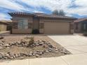 Tan single-story home featuring a tile roof, a two-car garage, and a gravel yard at 43857 W Bedford Dr, Maricopa, AZ 85138