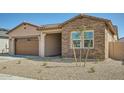 A view of the front of the home with a desert rock yard, walkway, and brick and stucco architectural details at 15053 W Gray Fox Trl, Surprise, AZ 85387