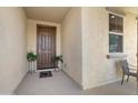 Inviting covered porch with a brown front door, neutral wall and accent plants at 21867 N 263Rd Dr, Buckeye, AZ 85396