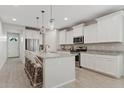 A modern, all-white kitchen offers an island with bar seating and stainless steel appliances for gourmet cooking at 9910 E Theia Dr, Mesa, AZ 85212