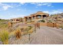 Grand Southwestern-style home features desert landscaping, a circular design, and a paved driveway leading to the gated entrance at 14360 E Desert Cove Ave, Scottsdale, AZ 85259