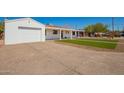 View of a white home with an attached garage, covered porch, manicured lawn, and a concrete driveway at 3028 E Highland Ave, Phoenix, AZ 85016