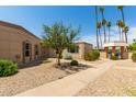 Exterior shot of a tan stucco home with desert landscaping, mature trees and shrubbery and several palm trees at 13677 N 108Th Dr, Sun City, AZ 85351