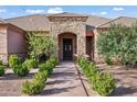 Charming entrance to a single story home with a stone archway, complemented by manicured shrubs and a paved walkway at 1096 W Via De Palmas --, San Tan Valley, AZ 85140
