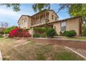 Charming two-story home with balcony, red flowers, lush greenery, and a classic brick retaining wall at 15239 W Alexandria Way, Surprise, AZ 85379