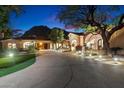 Well-lit home exterior featuring lush landscaping, a circular driveway, and a grand arched entrance at 6402 E Chaparral Rd, Paradise Valley, AZ 85253