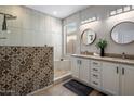 An updated bathroom with double sinks, white cabinets, a decorative-tiled shower, and a window at 2544 W Pumpkin Ridge Dr, Anthem, AZ 85086